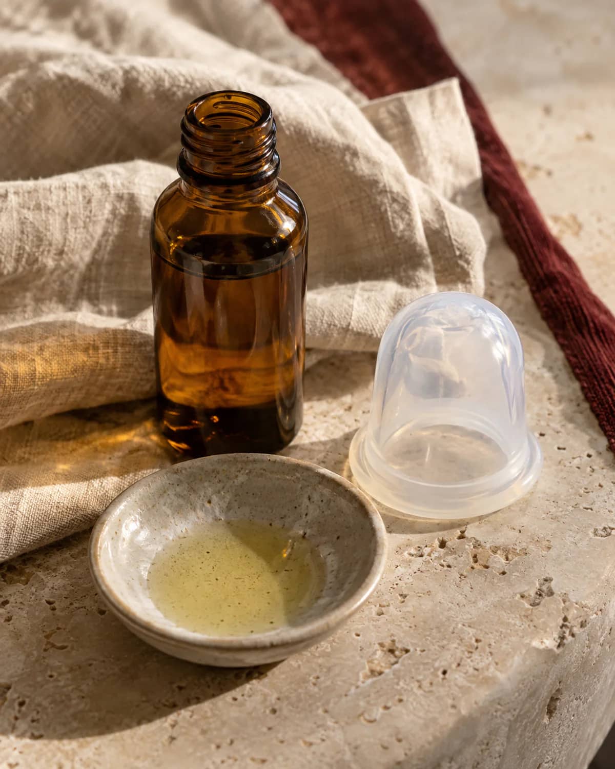 Macro shot of smooth natural massage oil in a glass bottle beside a single cup on warm linen